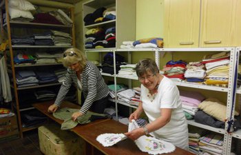 Foto: Eine ehrenamtliche Seniorin in der Kleiderkammer hält einen Stapel Kleidung und der Hand.